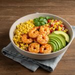 Final presentation of a grilled shrimp bowl with avocado, corn salsa, and creamy garlic sauce, perfect for a healthy dining experience.