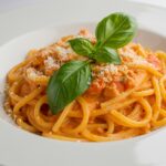 Final presentation of creamy tomato pasta garnished with basil and parmesan, showcasing a delicious Italian dish.