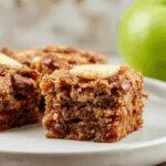 A slice of moist apple spice cake with a warm golden-brown crumb, topped with a dusting of cinnamon and nestled on a rustic white plate. The cake reveals tender bits of spiced apple, with a slightly textured topping and a hint of caramelization around the edges, set against a softly blurred background that emphasizes its inviting, homemade appeal.